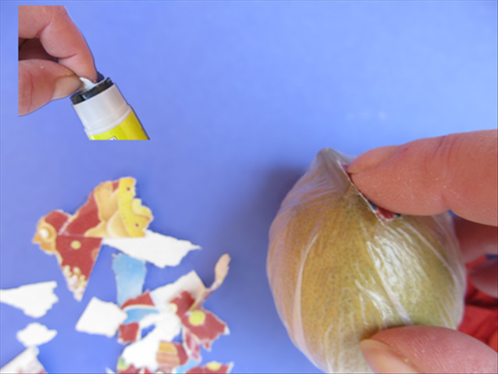Take one of the ripped papers and slide it across the top of the glue stick to coat the bottom with glue.
Press it against top of the lemon.
