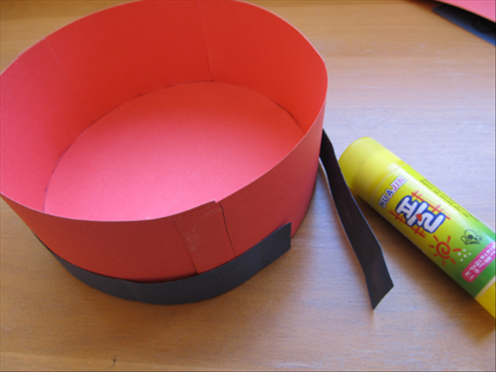 Glue together 1 inch wide strips to be long enough to go around the hat.

Place the circle side of the hat on the table and glue the strip around it.

