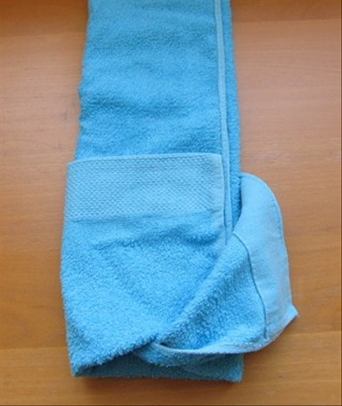 Rotate the towel so that the edge with the pocket is at the bottom.

At the bottom pull the second layer to the right and tuck the edge of the top layer in all the way.


