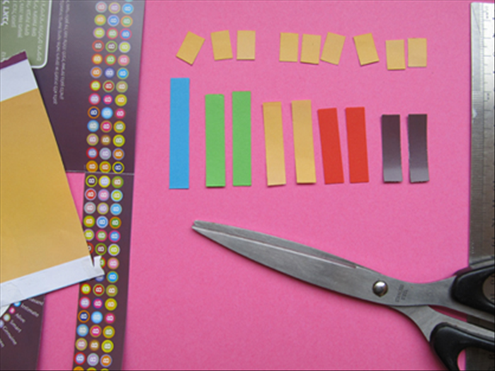 Cut out :
1 strip of paper  -  3/8 of an inch X  2 ½ inches       
2 strips of another color  -  3/8 of an inch X 2 ¼  inches      
2 strips of a different color -  3/8 of an inch X 2 inches     
2 strips of a different color -  3/8 of an inch X 1 ¾ inches  
2 strips of a different color -  3/8 of an inch X 1 ½ inches    
9 strips of a yellow or orange color  - 3/8 of an inch X 5/8 of an inch   
