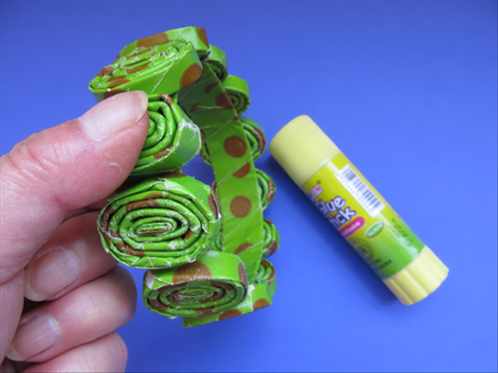 Apply a generous amount of paper glue to the bottom of the rolled paper.
Place it on the ring and hold it down a few seconds until it dries.
White glue takes too long and it will slide out of place. 
If you use hot glue that dries instantly skip the next step.
