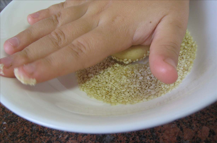 Put the sesame seeds on a plate

Press  the dough ball lightly down into the sesame seeds on each side

