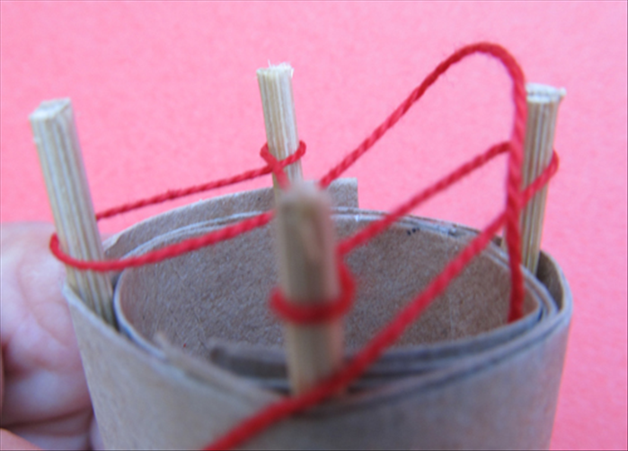 Pull the bottom string up over the top string and the stick.

You can do this with your fingers, a crochet needle or a toothpick

Now pull the string sticking out of the bottom of the tube. It will tighten the stitch
