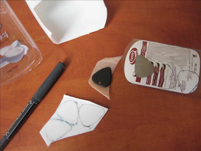 Make an outline of your store bought guitar pick on the plastic.

If you have lost all of them, draw an oval and make it pointy at the bottom.
