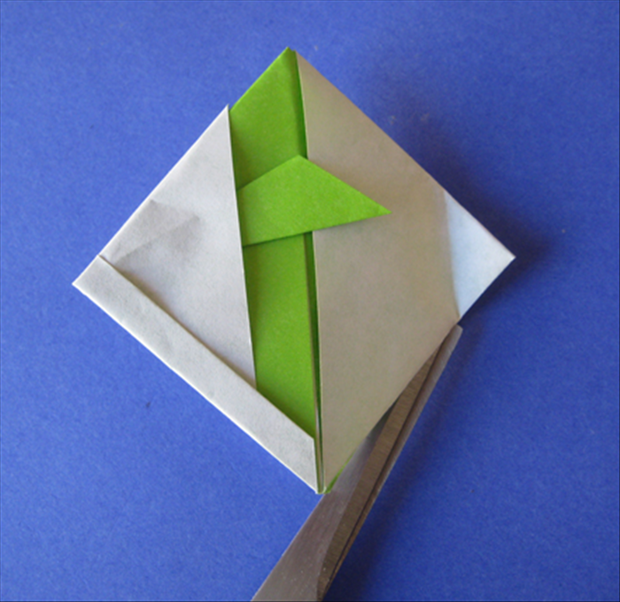 Lift the top layer and cut from the bottom point until the fold you just made. Do not cut all the way to the end.
 
Flip the paper over and cut the other side the same way – only until the crease. 
