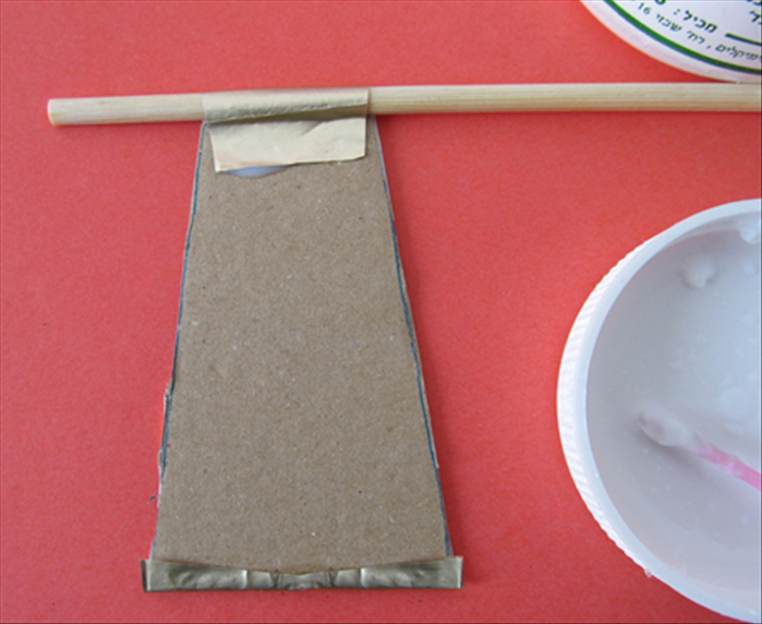 Put a chopstick on top of the paper  tab right above the cardboard piece and bring the paper up and over it. Glue only the area where the paper touches the cardboard. Pull the chopstick out. You should have a loop
Fold up the paper sticking out at the bottom and glue in place
