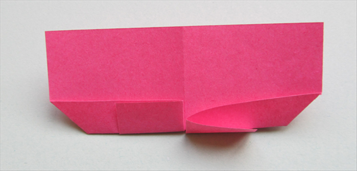 Flip the paper over to the back.

Pull out the top layer of the fold on the bottom right side

