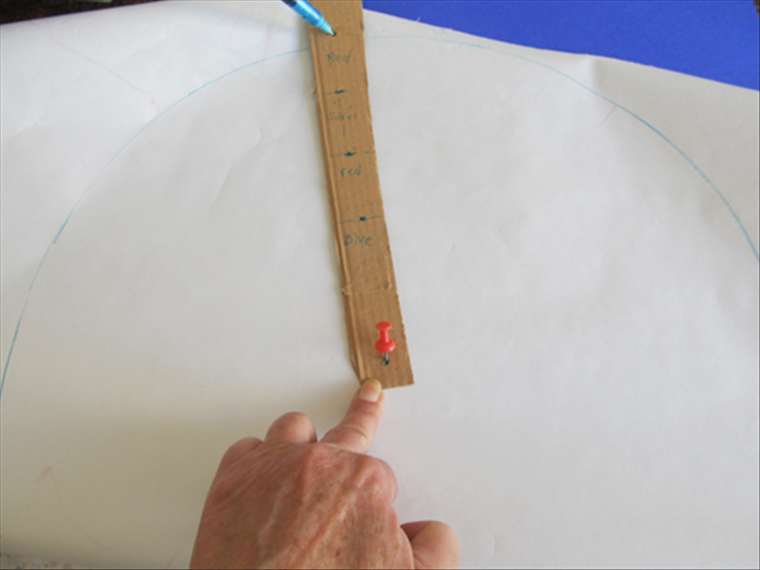 <p> Place the red paper color face down.</p> 
<p> Stick the push pin or nail through the bottom hole of the cardboard strip and through the center of the paper.</p> 
<p> Put the pen in the last hole at the top of the cardboard strip and rotate it to make a circle.</p> 
<p> Cut out the circle.</p> 
<p>  </p>