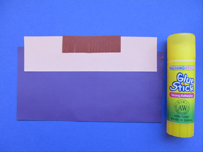 Align the paper for the bangs to the top and center of the skin colored paper and glue in place